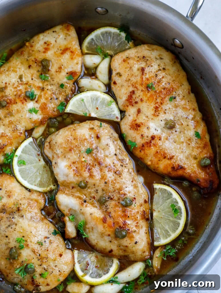 Overhead shot of lemon chicken piccata in a pot with lemon wedges. 