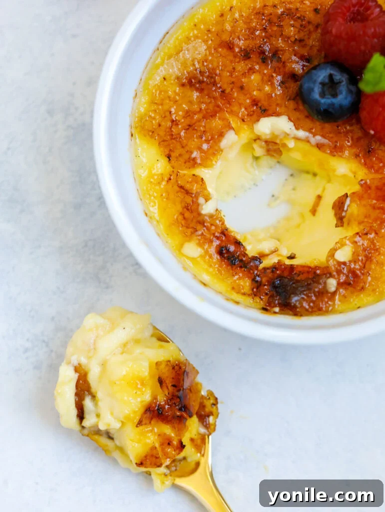 A close-up shot of an easy crème brûlée in a ramekin with a spoonful scooped out, showing the creamy interior and crunchy topping.
