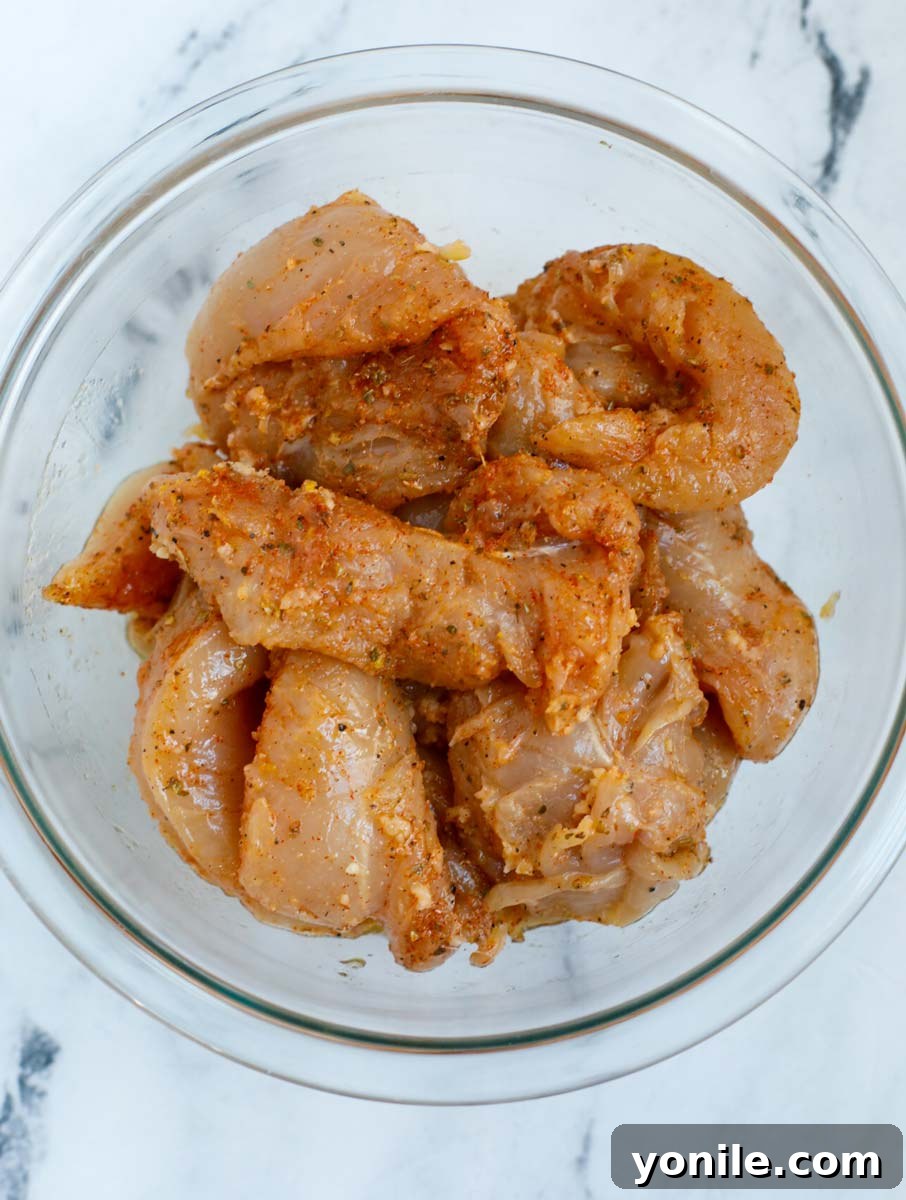 Crispy Air Fryer Lemon Pepper Chicken 4 Raw chicken tenders in a bowl with seasoning and lemon wedges.