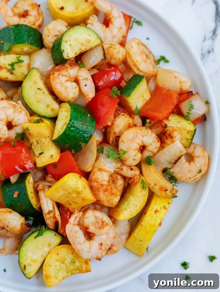 Top down shot of air fryer shrimp and vegetables on a plate, garnished with fresh herbs.