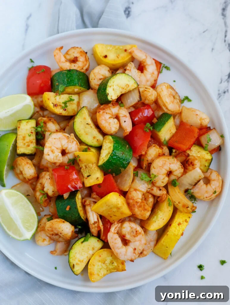 Top down shot of perfectly cooked air fryer shrimp and vegetables on a white plate, ready to be enjoyed.
