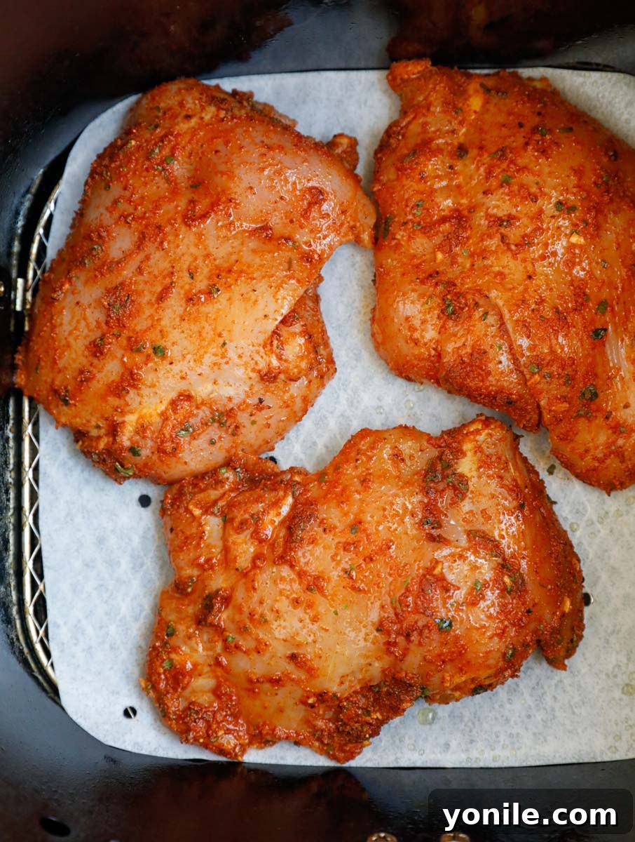 Crispy Air Fryer Chicken Thighs 6 Marinated raw chicken laid out in an air fryer basket.