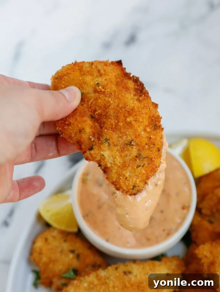 A crispy chicken strip being dipped into the special homemade sauce.