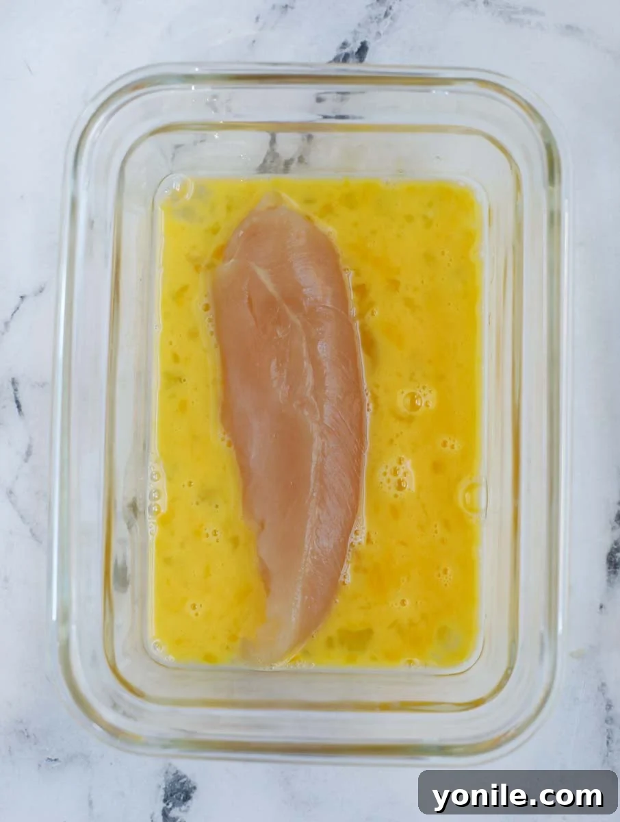Chicken tender being dipped into egg wash.