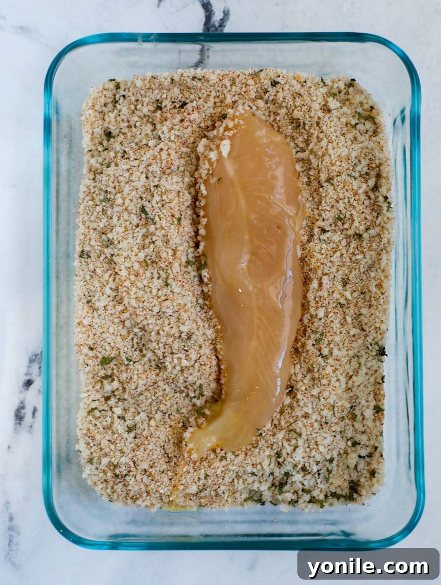 Chicken tender being coated in seasoned bread crumbs.