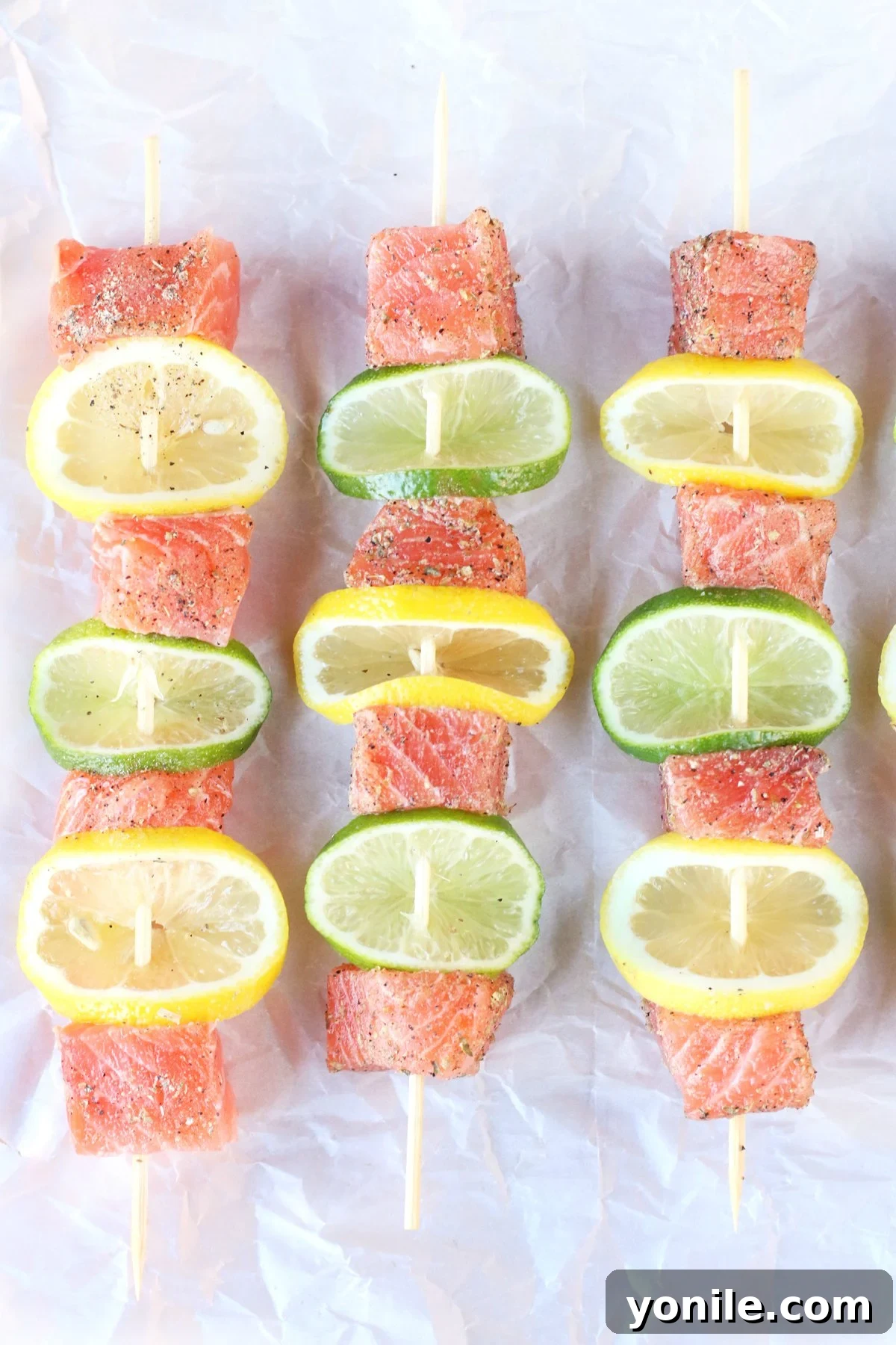 Raw salmon skewers with lemon and lime slices on a baking sheet, ready for the grill