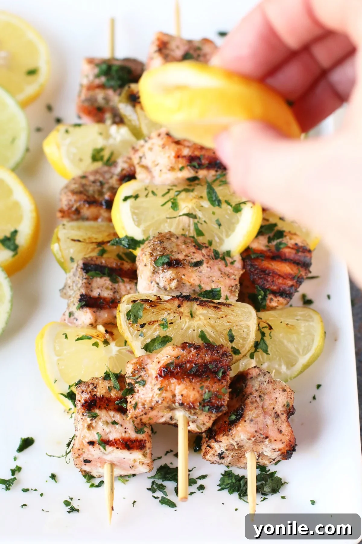 Squeezing fresh lime juice over a plate of hot grilled salmon skewers