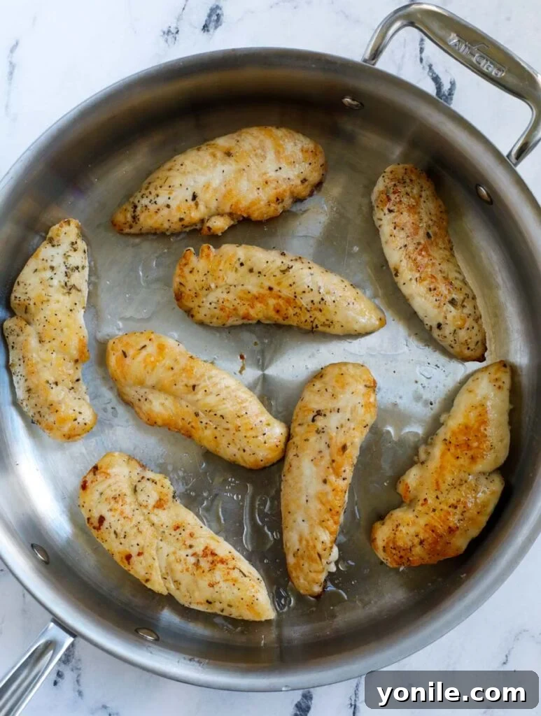 Top down shot of chicken tenders searing in a pan until golden brown.