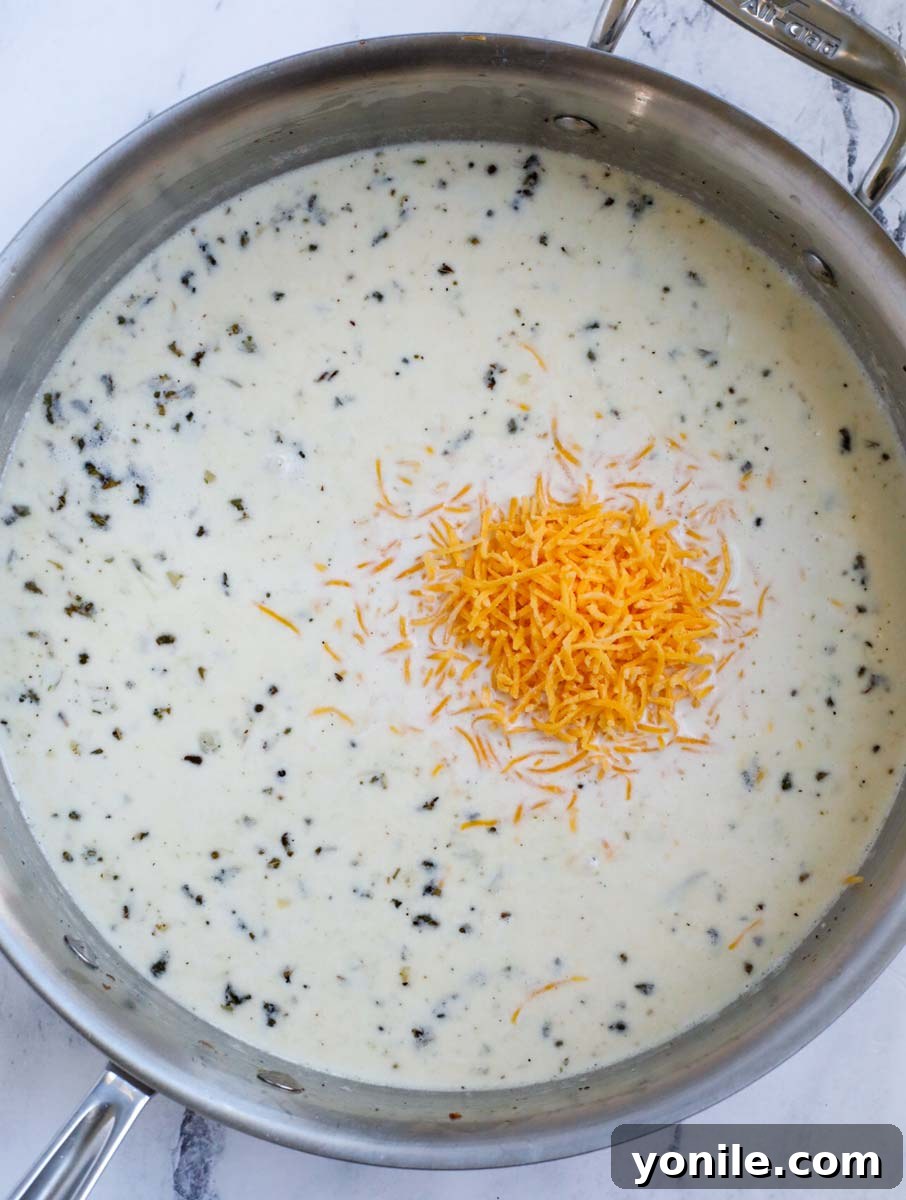 Stirring in shredded cheddar cheese into the simmering cream sauce until smooth.