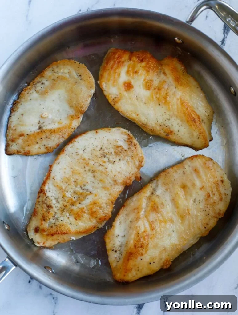 Dreamy Creamy Pesto Chicken 4 Close-up of chicken breasts pan-frying in a skillet until golden brown.