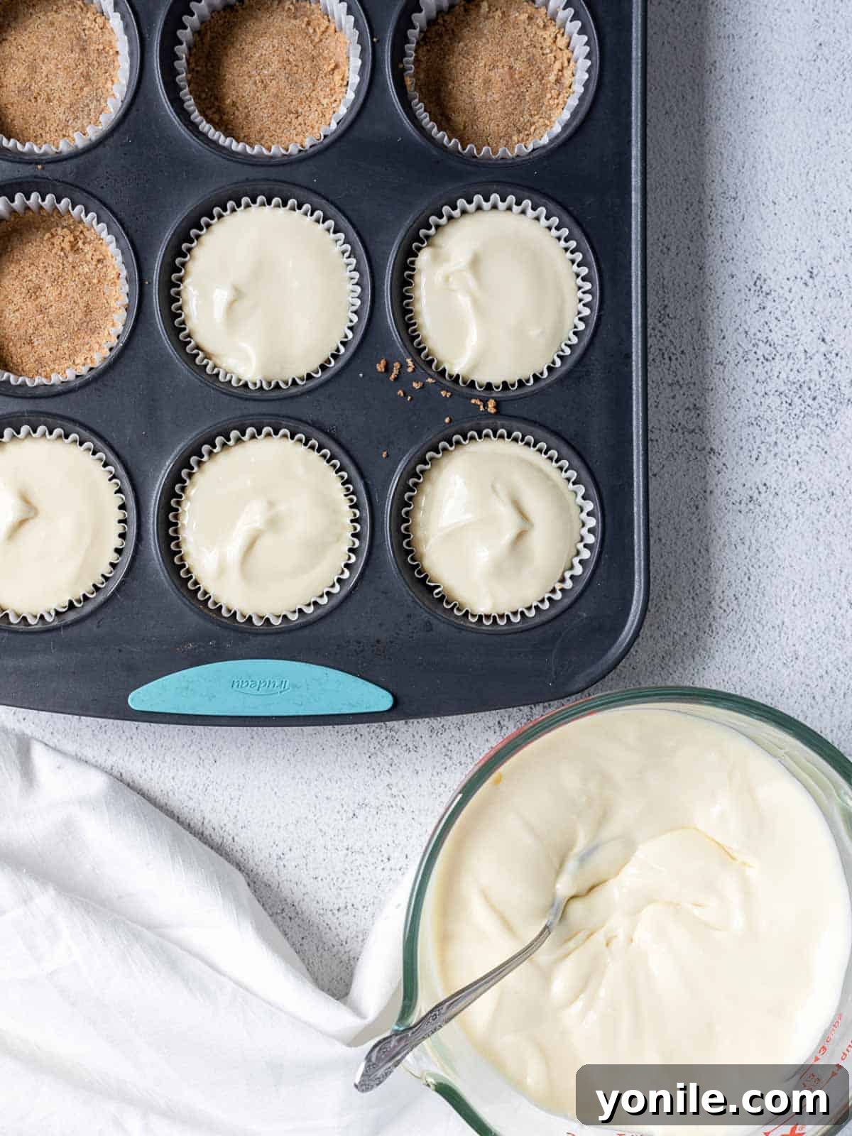 A cupcake tin filled with cheesecake batter in liners, ready for baking.