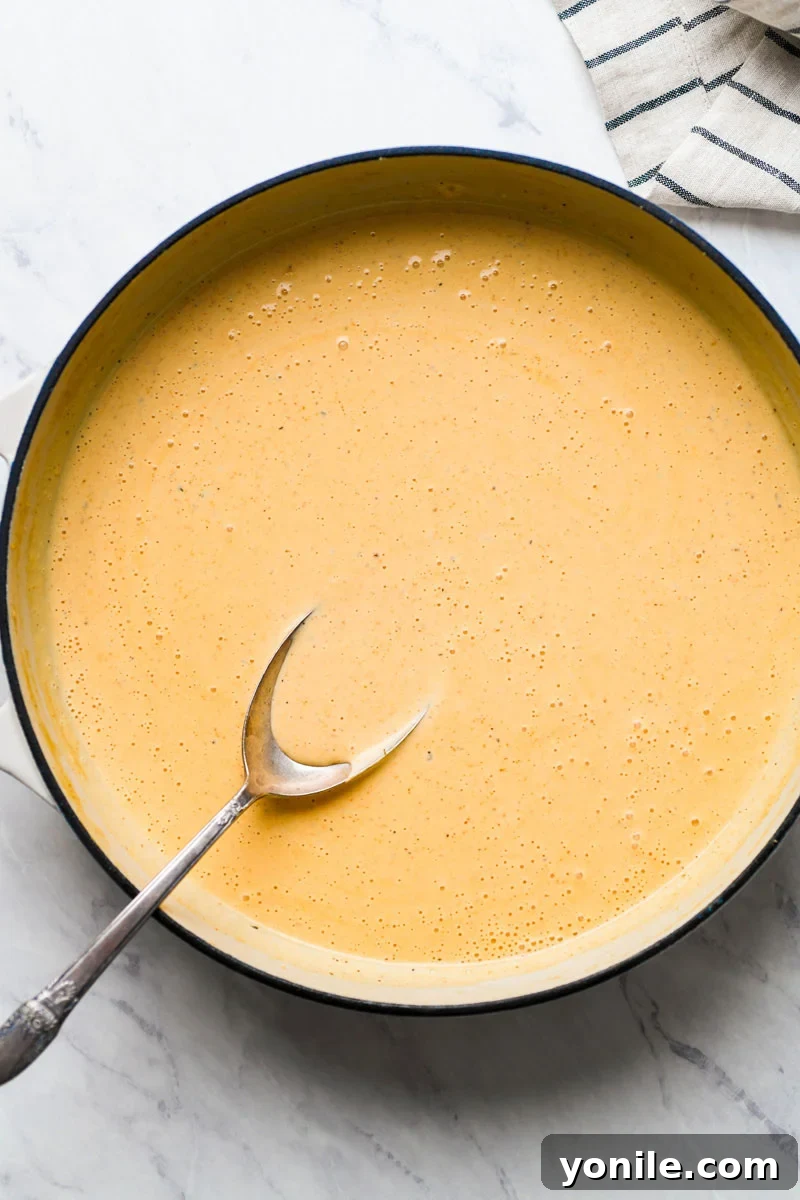 Close-up of a creamy, rich Cajun cheese sauce simmering in a skillet, ready for pasta and chicken.