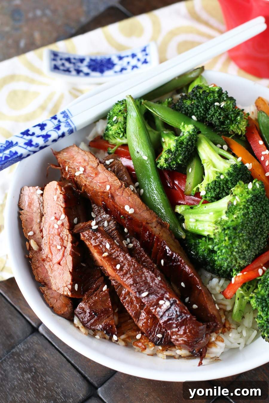 Sizzling Soy Flank Steak Stir-Fry 3 Image of soy marinated flank steak stir-fry with white and blue chopsticks on the bowl and a white and brown napkin in the back.