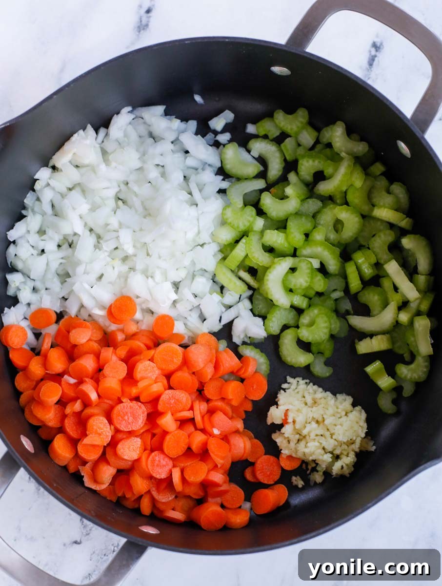 Freshly diced carrots, sliced celery, and chopped onions are being gently sautéed in olive oil within a large, gleaming stainless steel pot on a stovetop.