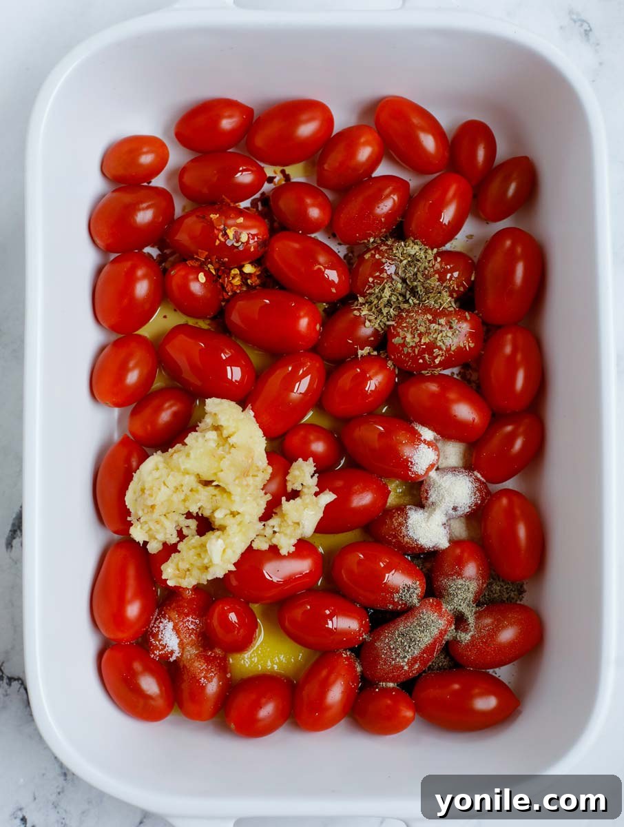 Cherry tomatoes seasoned with herbs and spices, drizzled with olive oil in a baking dish, ready for roasting.