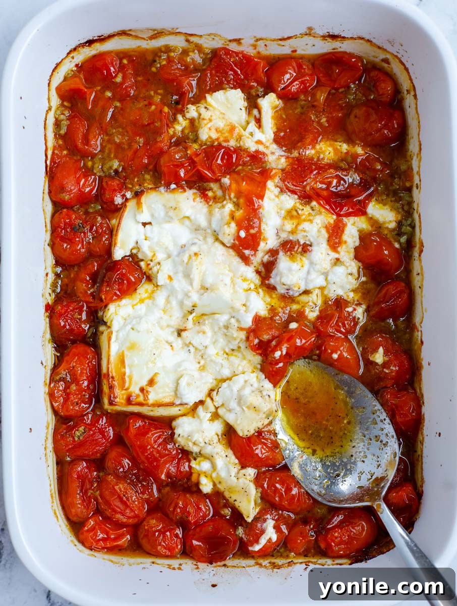 Mashing the melted feta and roasted tomatoes together in the baking dish to create a creamy sauce.