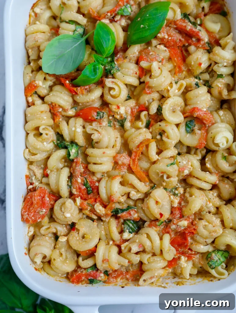 A large casserole dish filled with baked feta pasta, generously garnished with fresh basil, ready for a family meal.