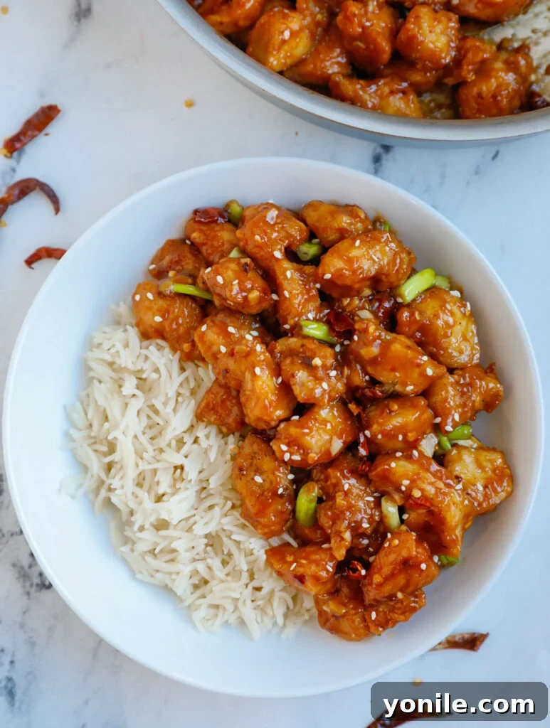 No Fuss General Tsos Chicken 13 Overhead image of a bowl of General Tso's chicken with a side of steamed white rice, garnished with green onions and sesame seeds.