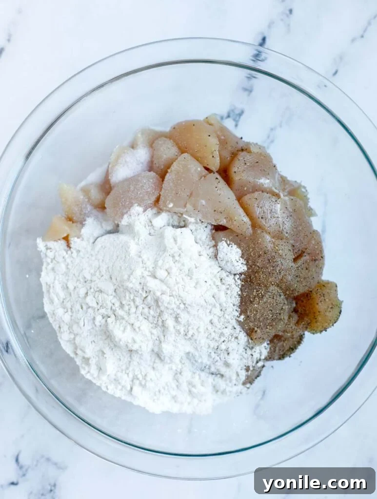 No Fuss General Tsos Chicken 5 Chicken being added to a bowl with flour, salt, and pepper for coating.