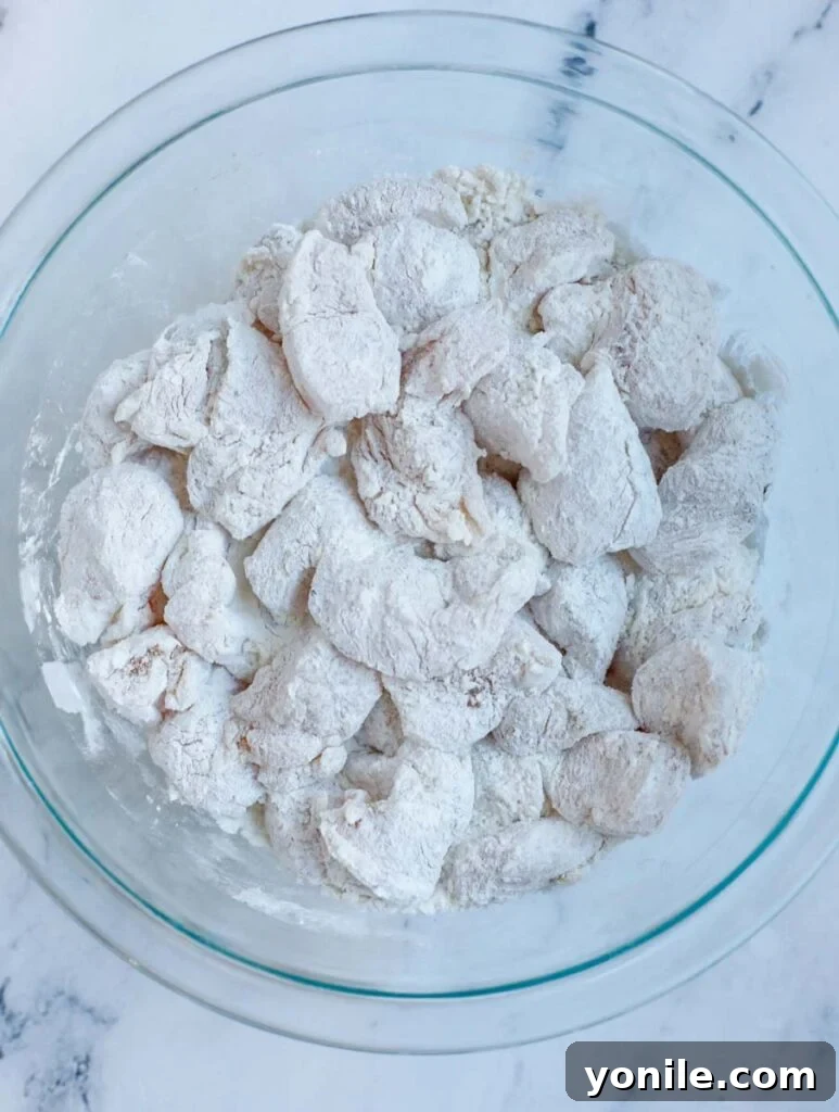 No Fuss General Tsos Chicken 6 Chicken pieces being covered thoroughly in the flour mixture.