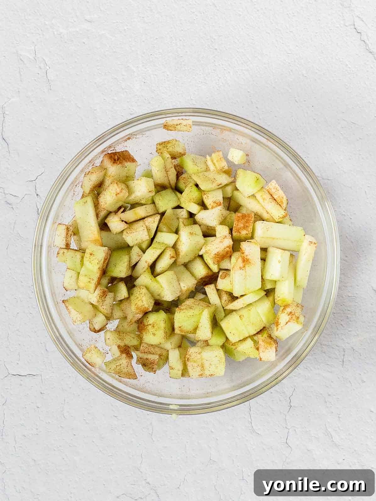 Neatly cubed green apple pieces, lightly dusted with cinnamon, in a small bowl.