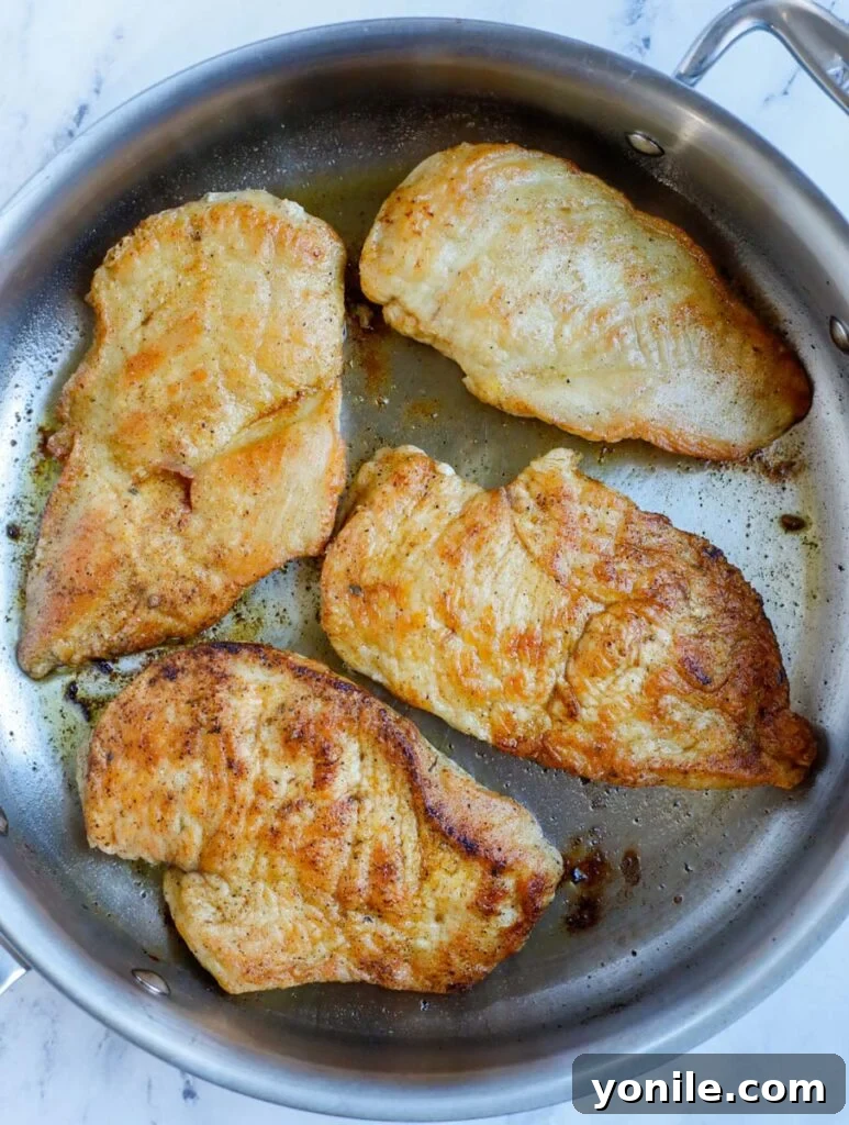 Two pieces of seasoned chicken breast sizzling and turning golden brown in a hot skillet with olive oil.