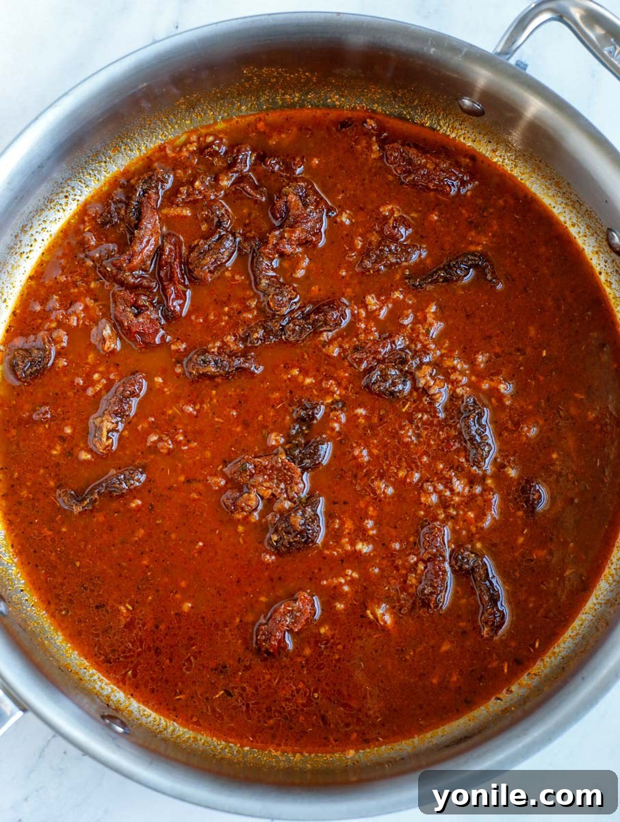 Chipotle pepper sauce, chicken broth, and sun-dried tomatoes introduced into the skillet with sautéed spices, forming the base of the creamy Cajun sauce.