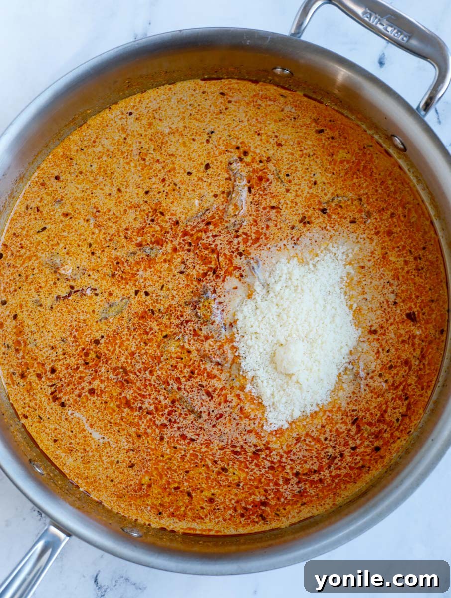 Grated Parmesan cheese being stirred into the simmering Cajun cream sauce, adding richness and helping it to thicken beautifully.