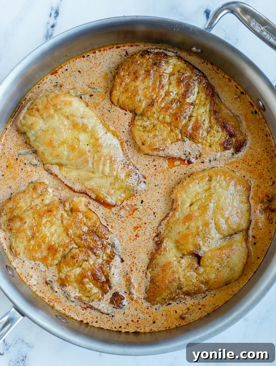 Perfectly cooked creamy Cajun chicken breasts nestled in a skillet, thoroughly coated in the rich, savory sauce.