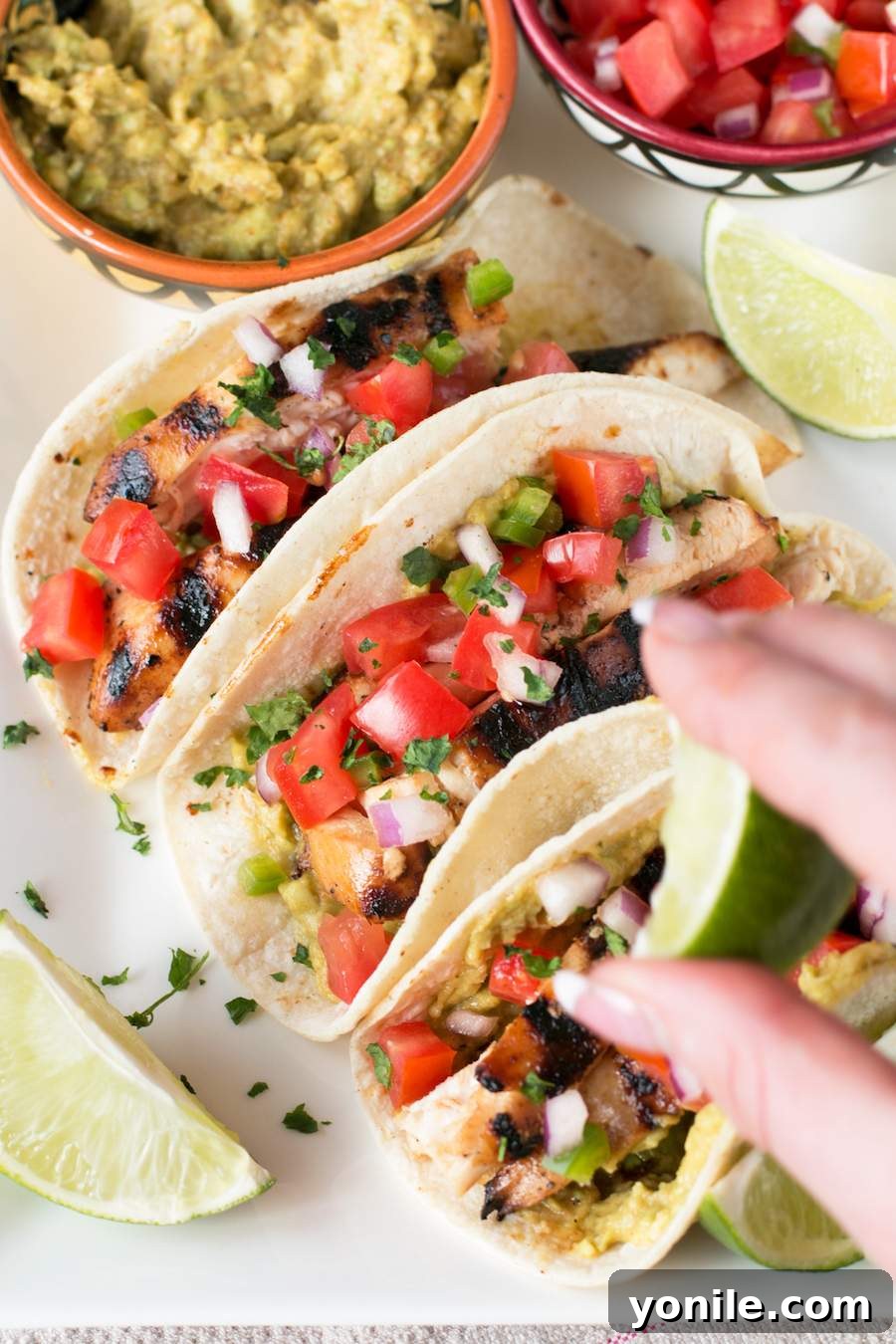 A hand squeezing fresh lime juice over three assembled Mexican Chicken Tacos, enhancing their flavor.
