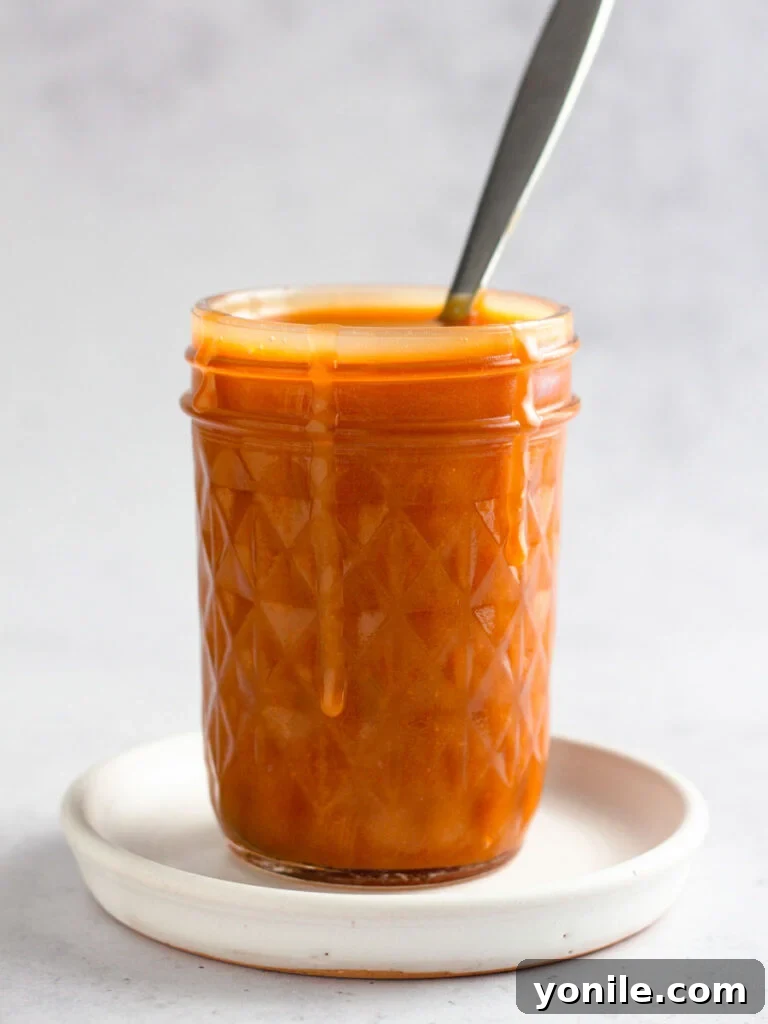 A mason jar filled with freshly made homemade caramel sauce, cooling on a wooden surface, ready to be stored or served.