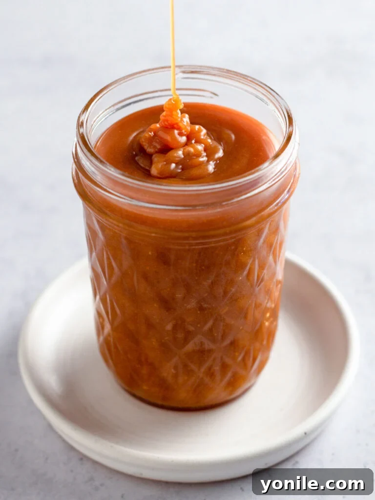 A beautifully textured homemade caramel sauce in a clear glass mason jar, showcasing its rich golden color and inviting consistency, ready for use.