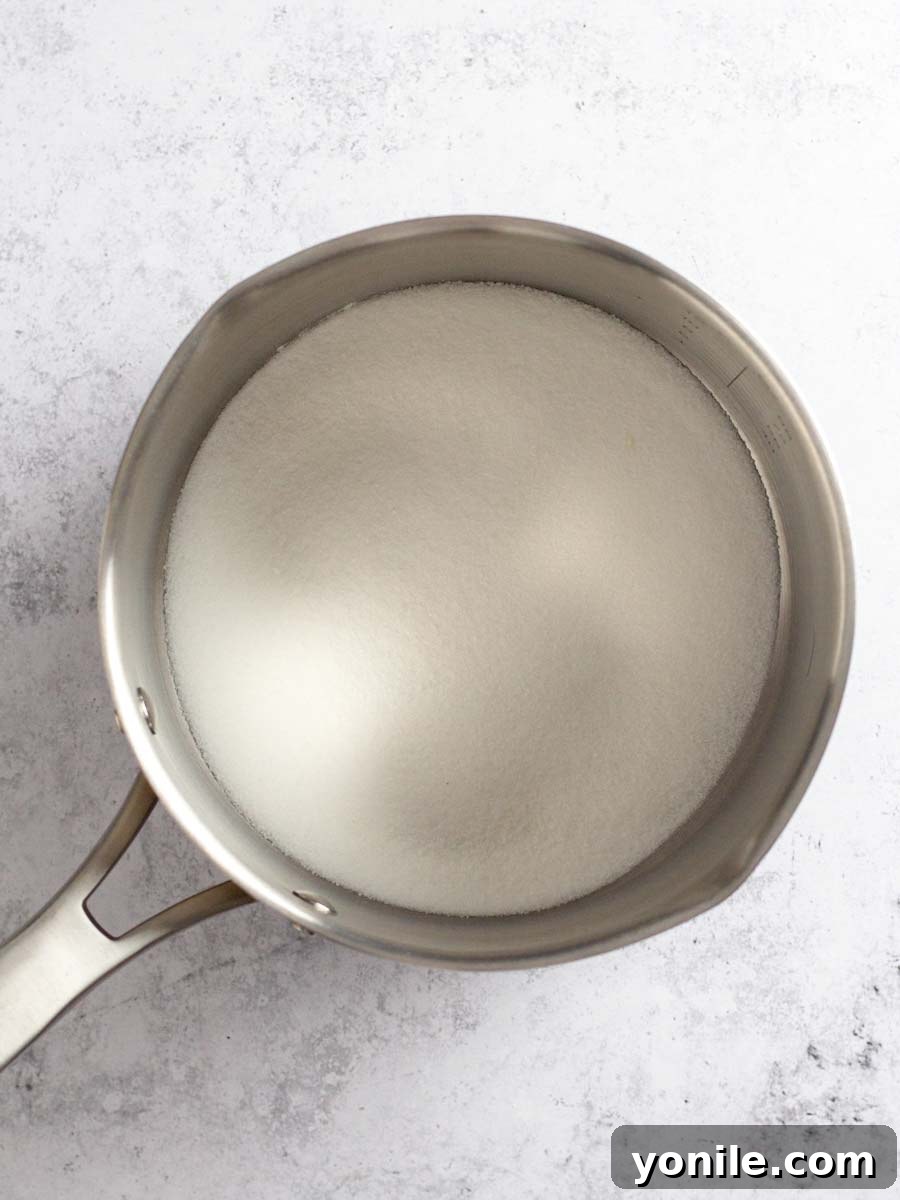 Granulated sugar evenly spread at the bottom of a large, light-colored saucepan, ready for caramelization.
