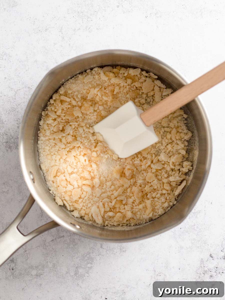 Sugar beginning to melt and form golden clumps in a saucepan over medium heat, indicating the start of caramelization.