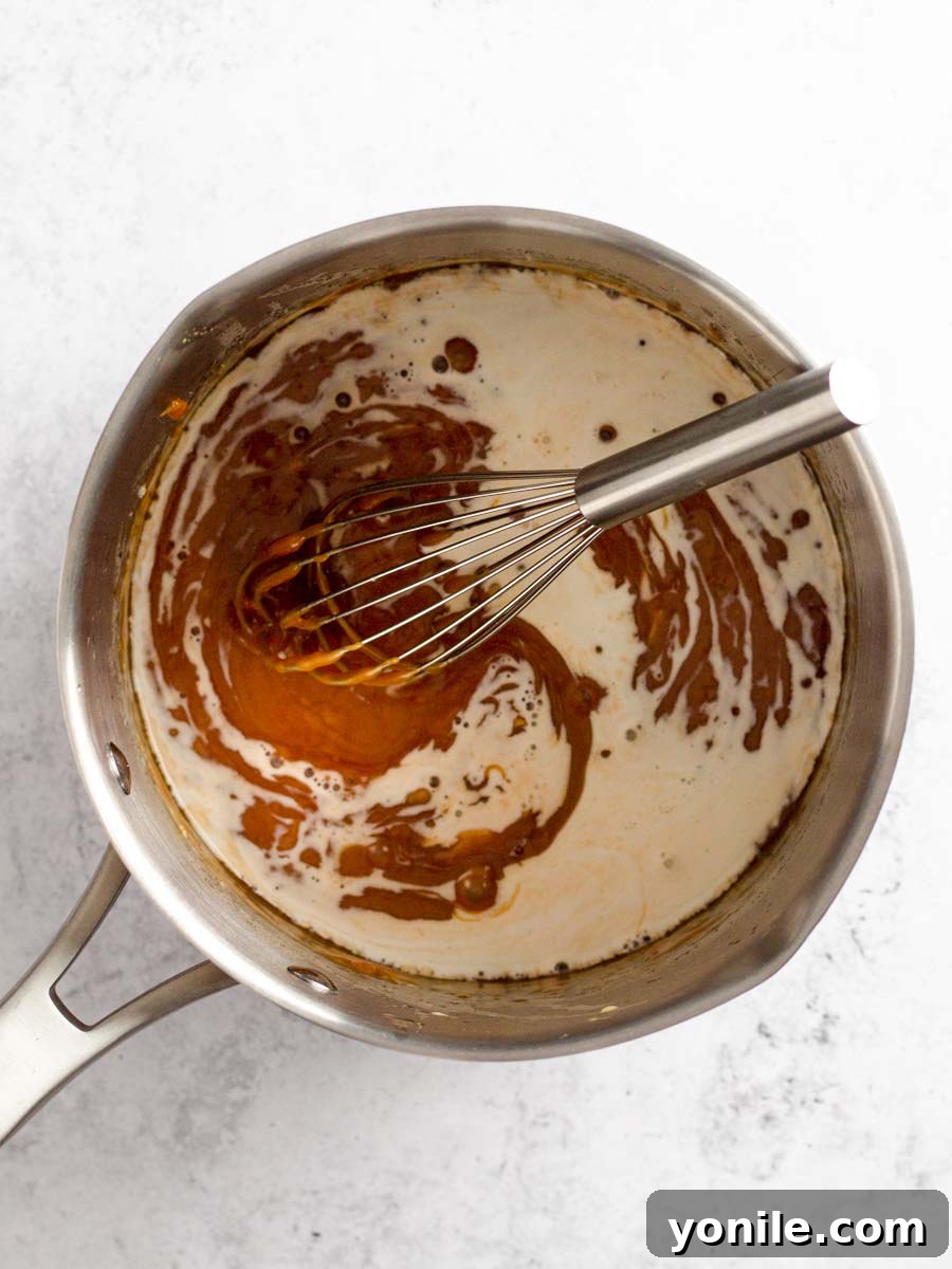 A whisk blending the caramel sauce in a saucepan, showing a smooth, cohesive mixture after the cream has been added.