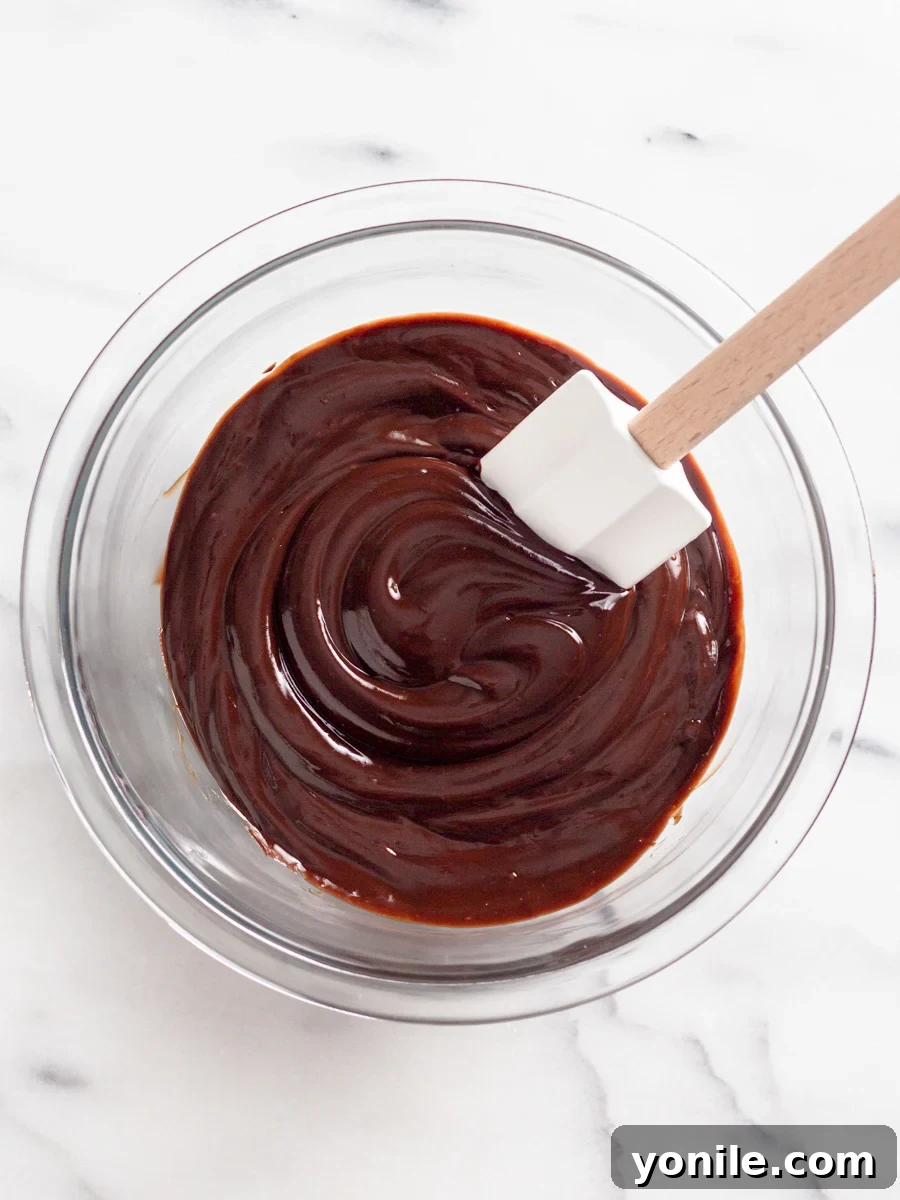 Mastering Chocolate Ganache 6 A rubber spatula is gently stirring the chocolate and cream mixture, transforming it into smooth ganache.
