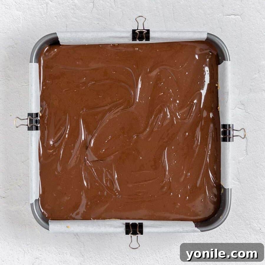 Decadent Chocolate Peanut Butter Oat Bars 7 The assembled chocolate peanut butter oatmeal bars in a square pan, with the melted chocolate topping spread over the oat base.