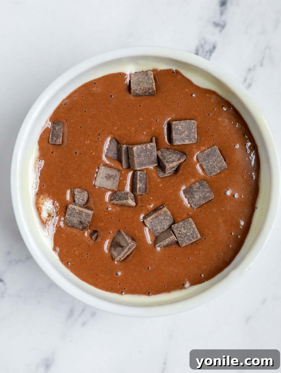 Chocolate peanut butter baked oats batter in a ramekin with chocolate chunks on top.
