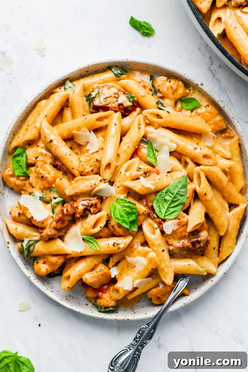 A plate of creamy sun-dried tomato pasta with fresh basil and parmesan shavings on top, ready to be served.