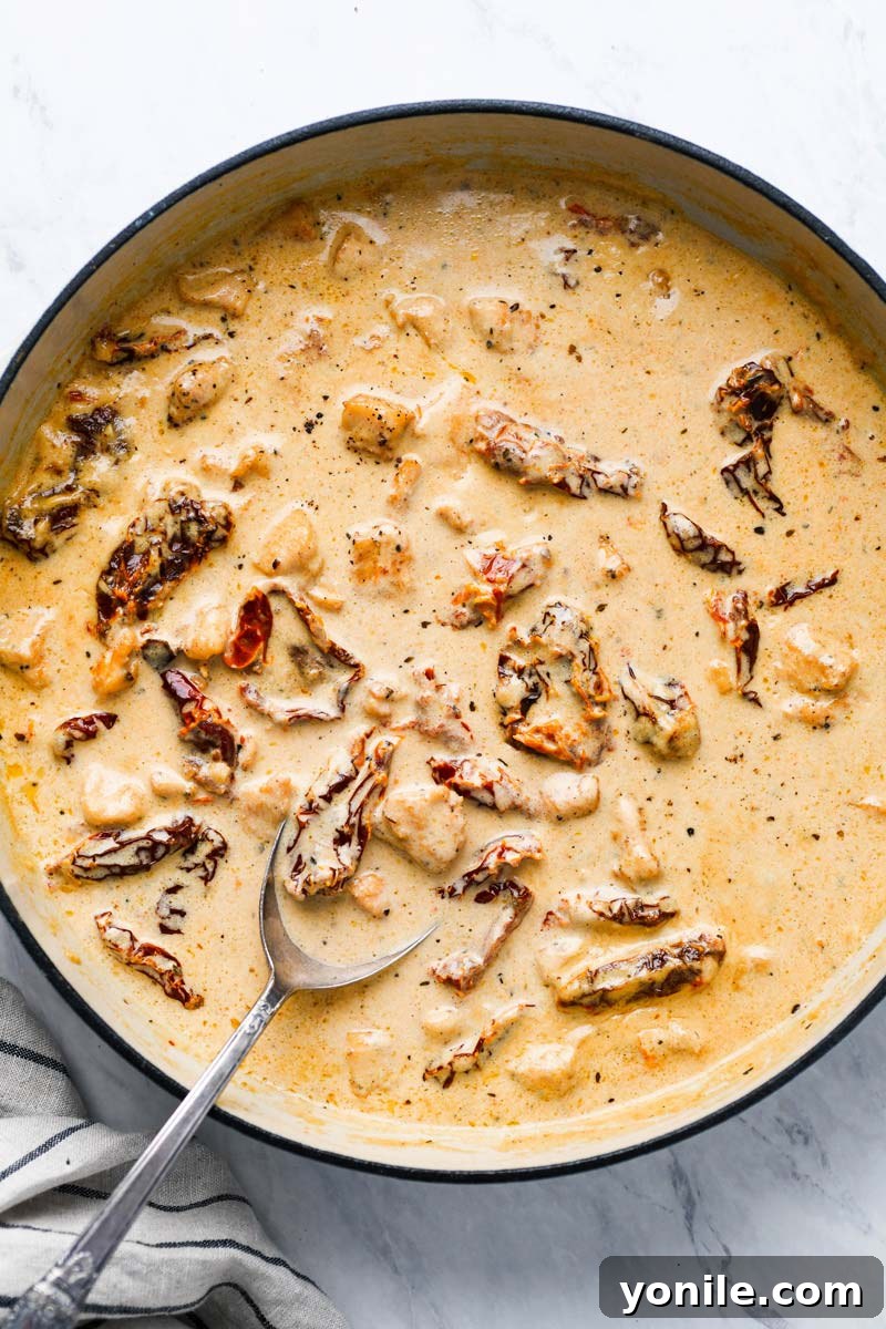 Sauce being made in a pot for sun-dried tomato pasta, with creamy texture and visible tomatoes.