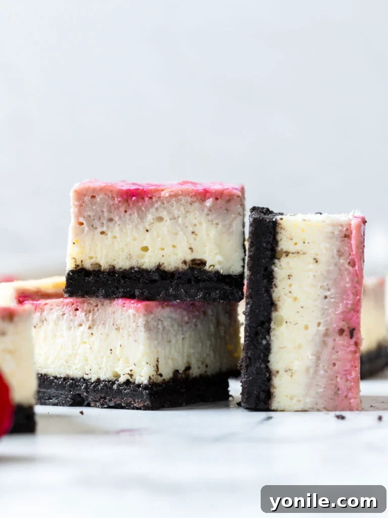 Luscious Raspberry Cheesecake Bars 2 Two generously sized raspberry cheesecake bars stacked, with another bar beside them, showcasing the vibrant raspberry swirl and thick Oreo crust.