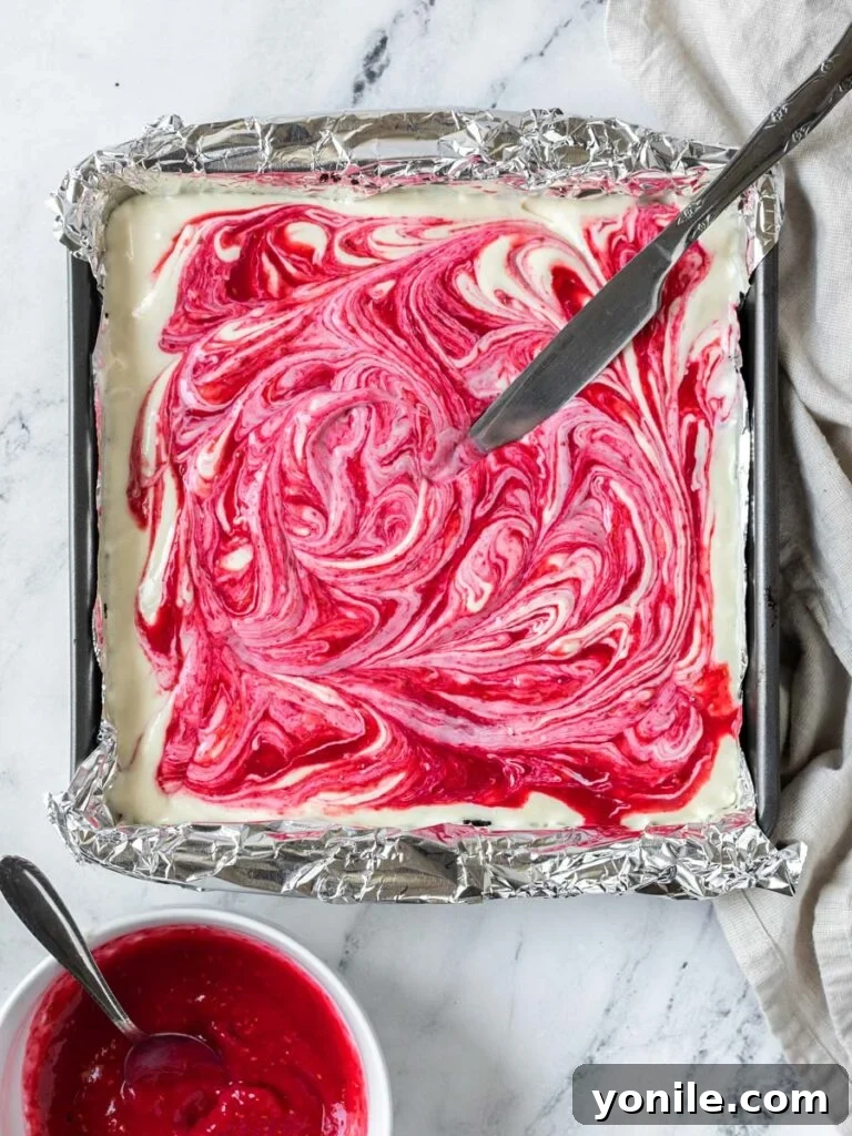 Luscious Raspberry Cheesecake Bars 3 A top-down view of the cheesecake filling poured over the Oreo crust in a square baking pan, ready for the raspberry swirl.