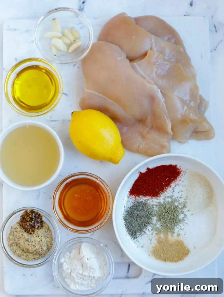 Sweet & Tangy Mustard Chicken 3 An overhead shot showcasing the fresh ingredients for honey mustard chicken laid out on a kitchen counter, including chicken breasts, honey, Dijon mustard, spices, and lemon.