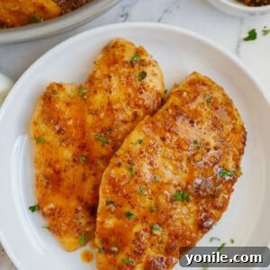 A plate of perfectly seared honey mustard chicken breasts, drizzled with the rich, golden sauce and garnished with fresh herbs.