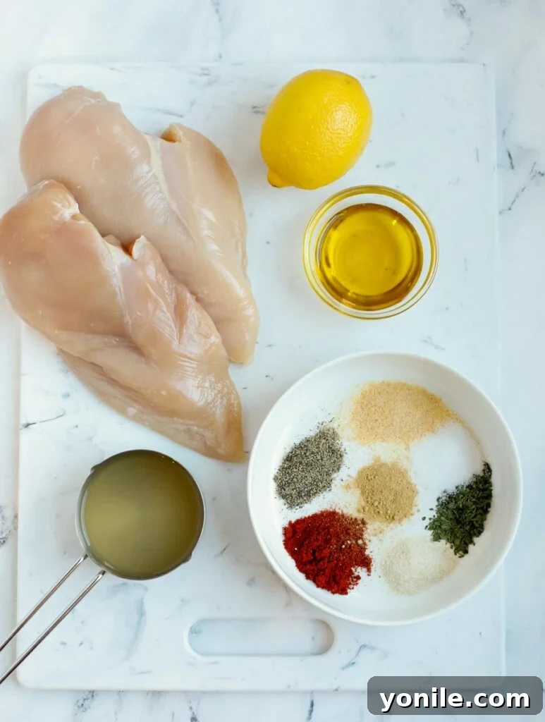 An overhead shot showcasing all the fresh and aromatic ingredients meticulously laid out for preparing oven baked chicken breasts: chicken, lemon, fresh herbs, and various spices.