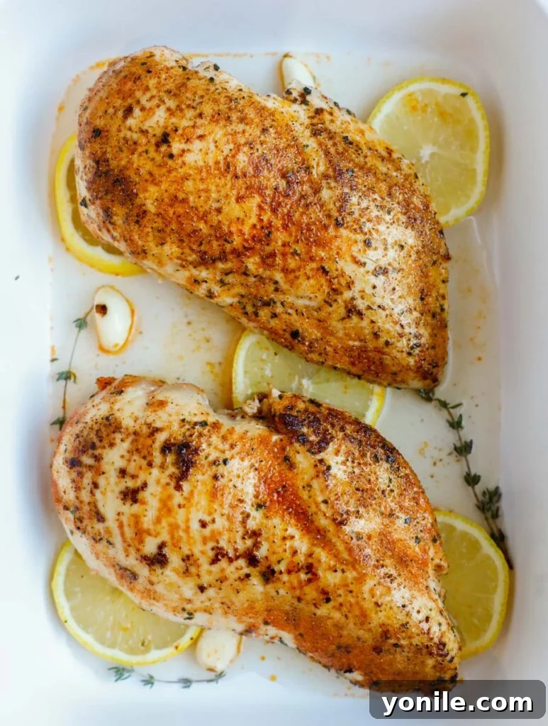 Perfectly seasoned oven-baked chicken breasts nestled in a baking dish with lemon and herbs, fresh out of the oven.