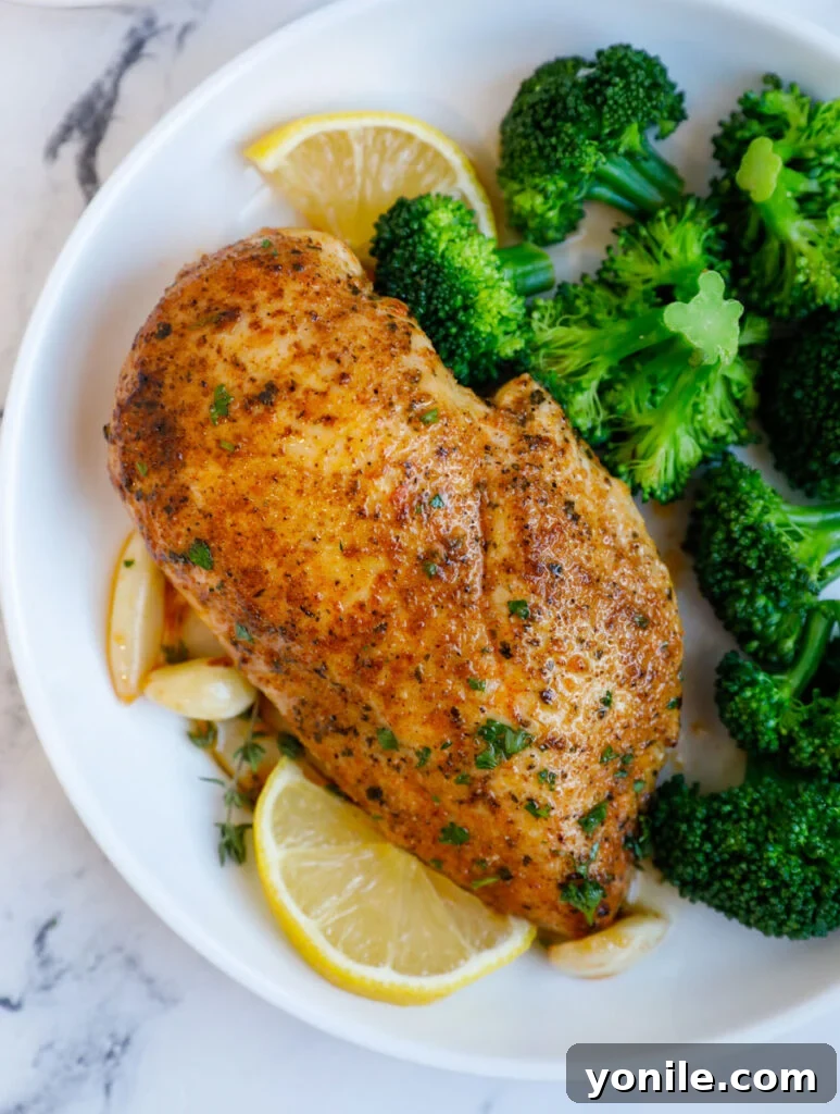 A perfectly cooked oven-baked chicken breast, sliced to reveal its juicy interior, served alongside vibrant green broccoli florets for a complete, healthy meal.