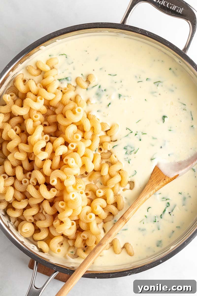 Velvety Spinach Macaroni and Cheese 6 Cooked cavatappi macaroni pasta being gently mixed into the creamy spinach cheese sauce, ensuring every piece is coated.