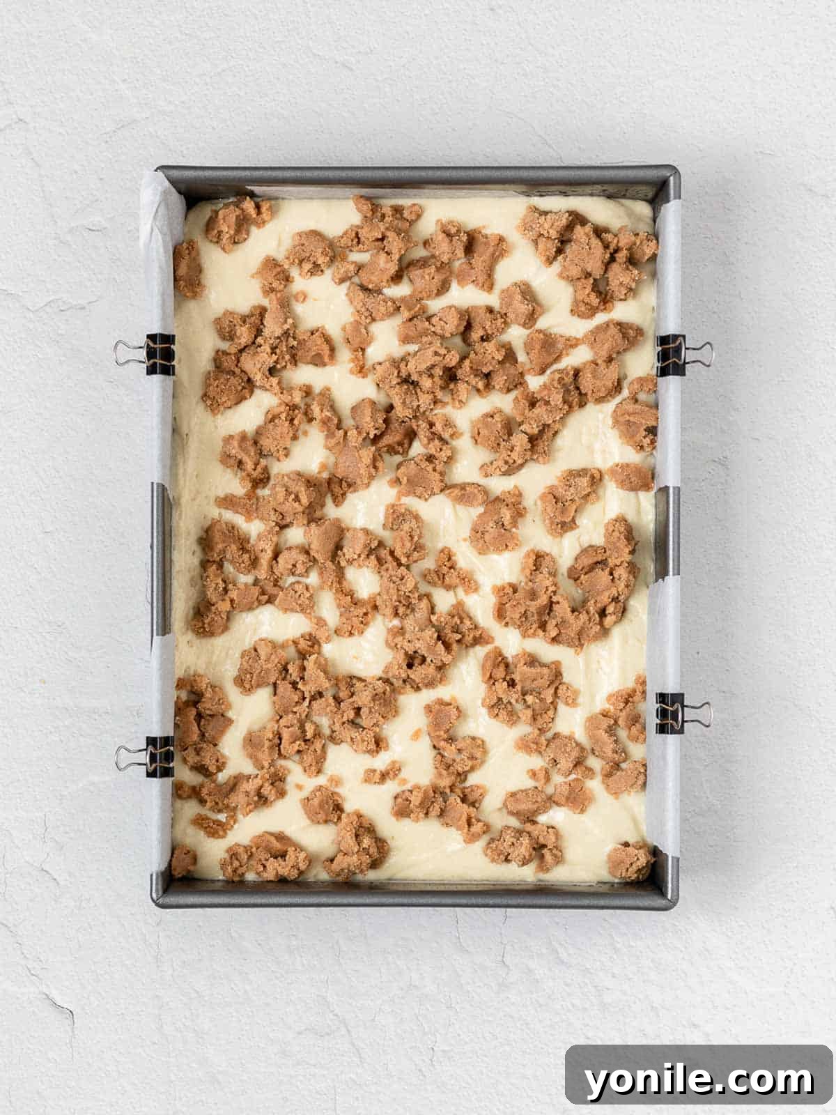 Uncooked coffee cake batter in a baking pan, generously topped with a homemade cinnamon streusel mixture, ready for the oven.