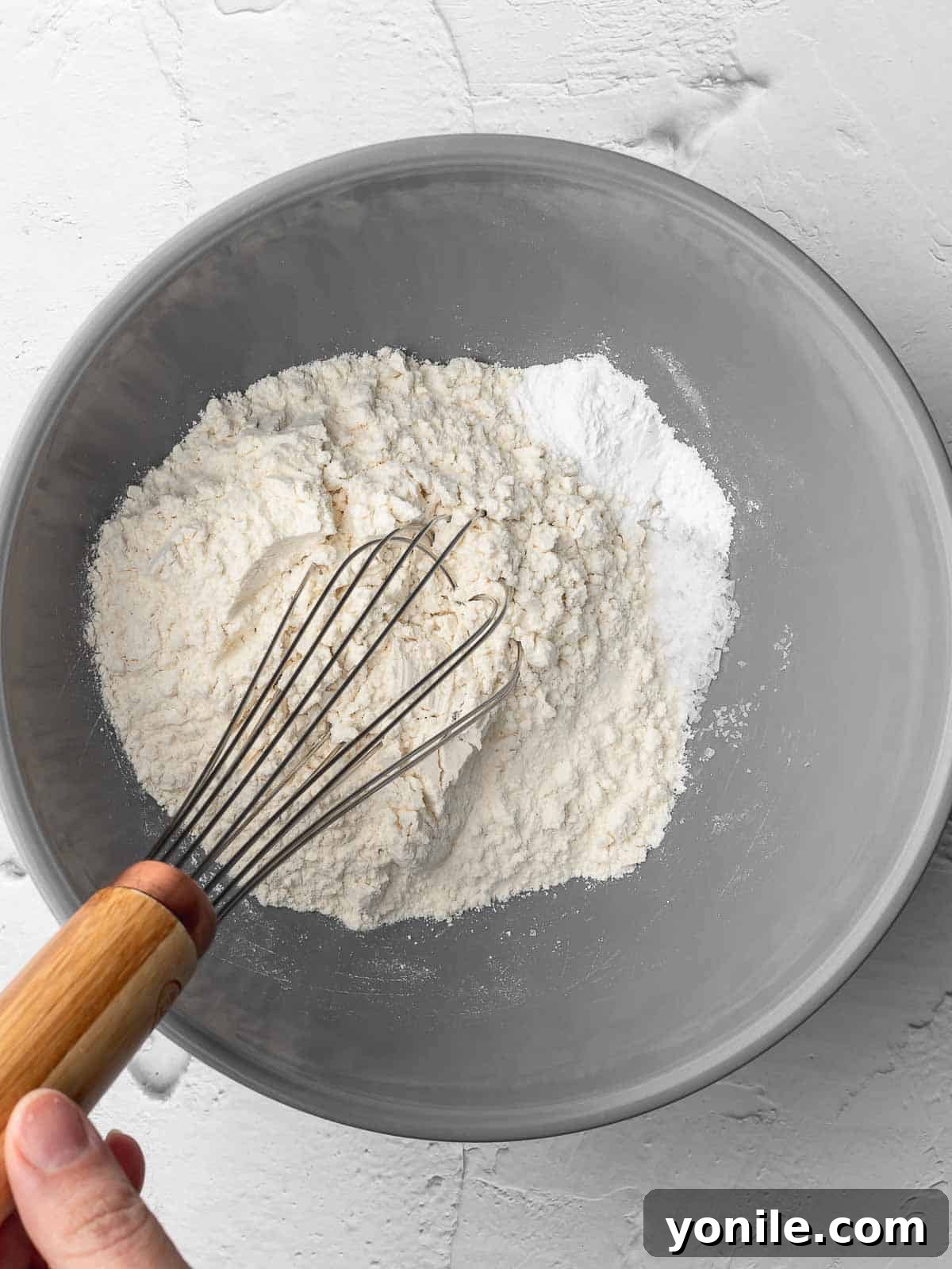 A bowl containing mixed dry ingredients (flour, salt, baking powder) for crispy almond oatmeal cookies.